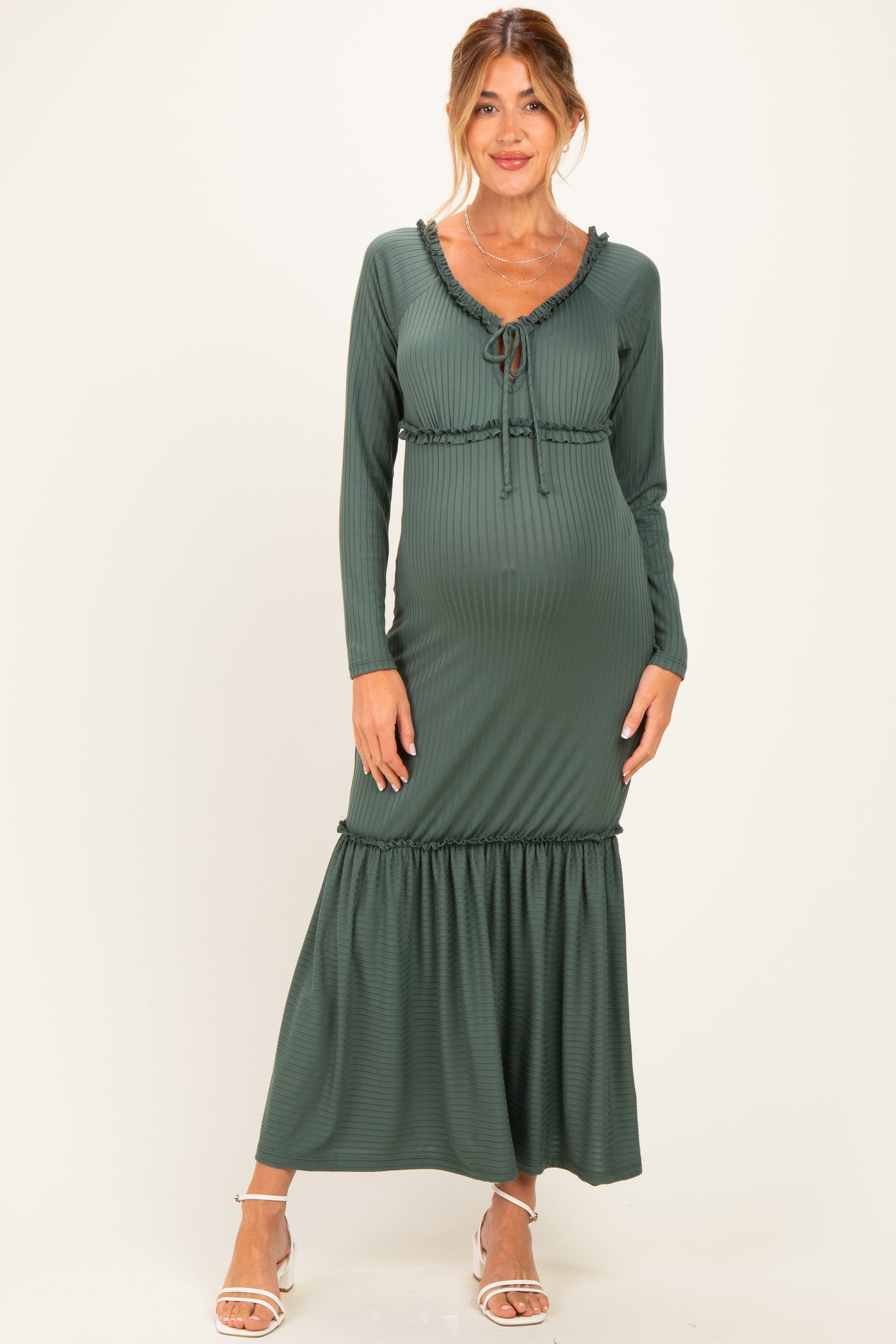 woman wearing a dark green maternity maxi dress with long sleeves and ruffle detailing, showing her baby bump