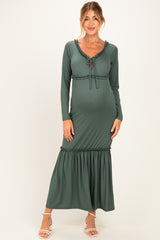 woman wearing a dark green maternity maxi dress with long sleeves and ruffle detailing, showing her baby bump