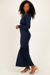 woman wearing a navy ribbed maxi dress with long sleeves and ruffled hem, posing sideways with curly hair