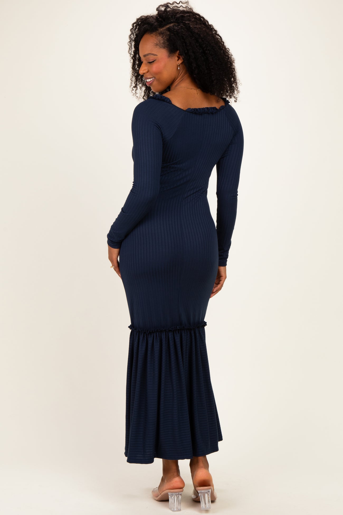 woman wearing a dark blue ribbed maxi dress with long sleeves and a ruffled hem, shown from the back
