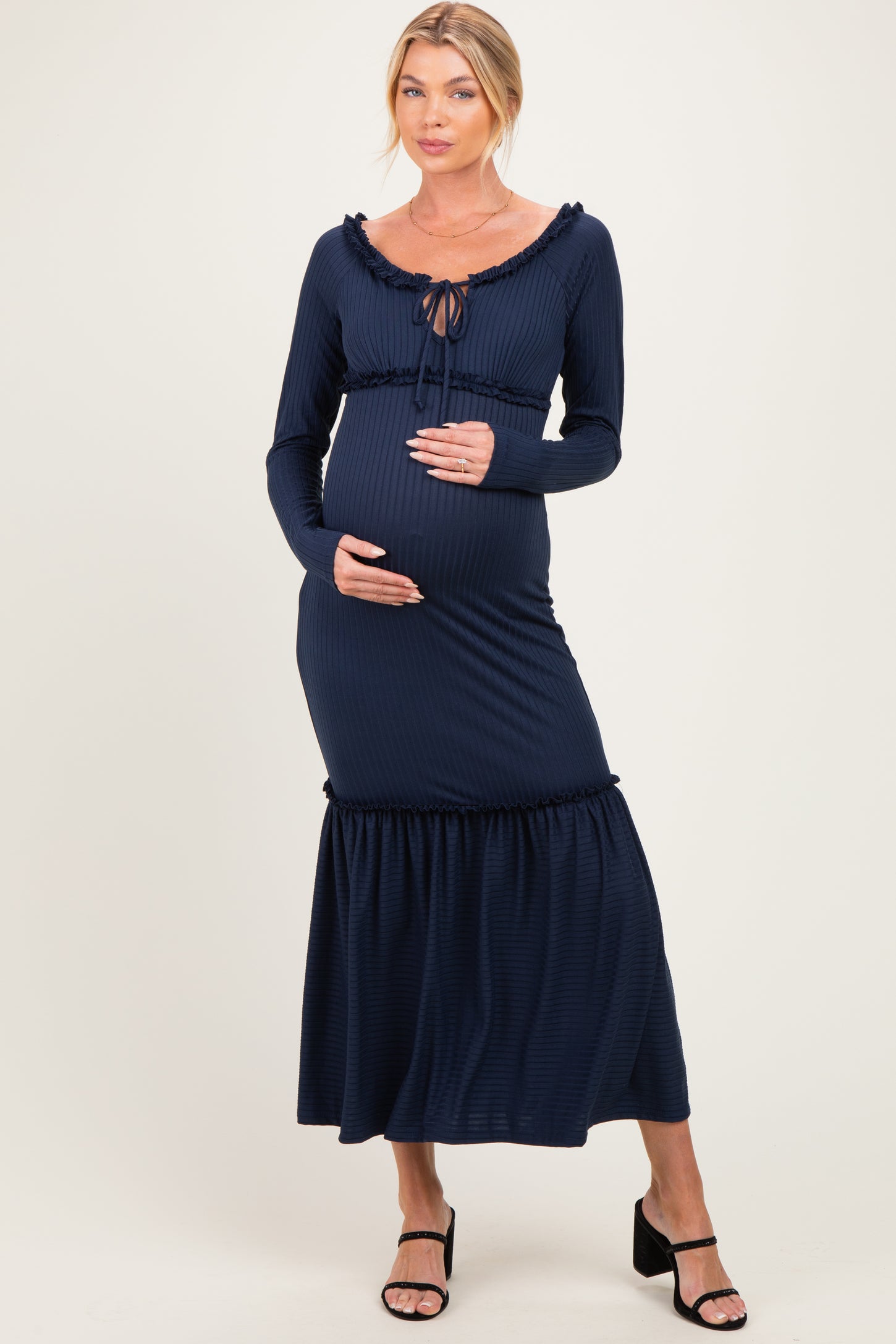 woman wearing a navy blue maternity dress with long sleeves and a ruffled hem, holding her baby bump