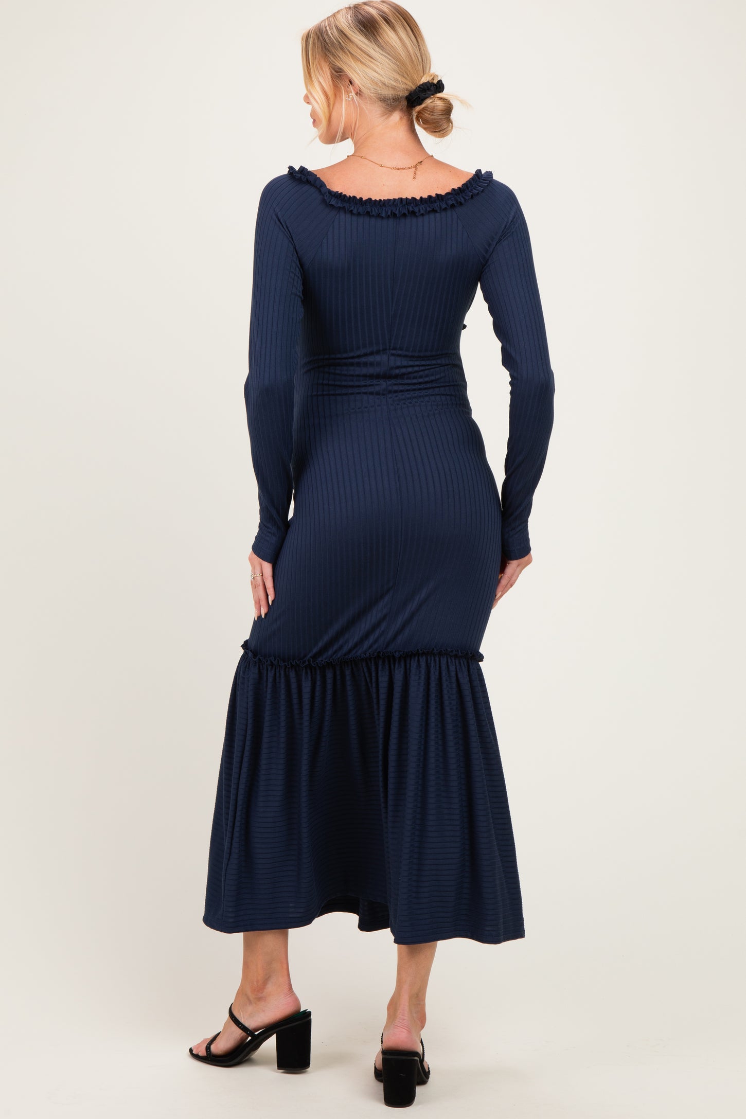 woman wearing a navy blue ribbed maternity dress with a ruffled hem and long sleeves, seen from the back