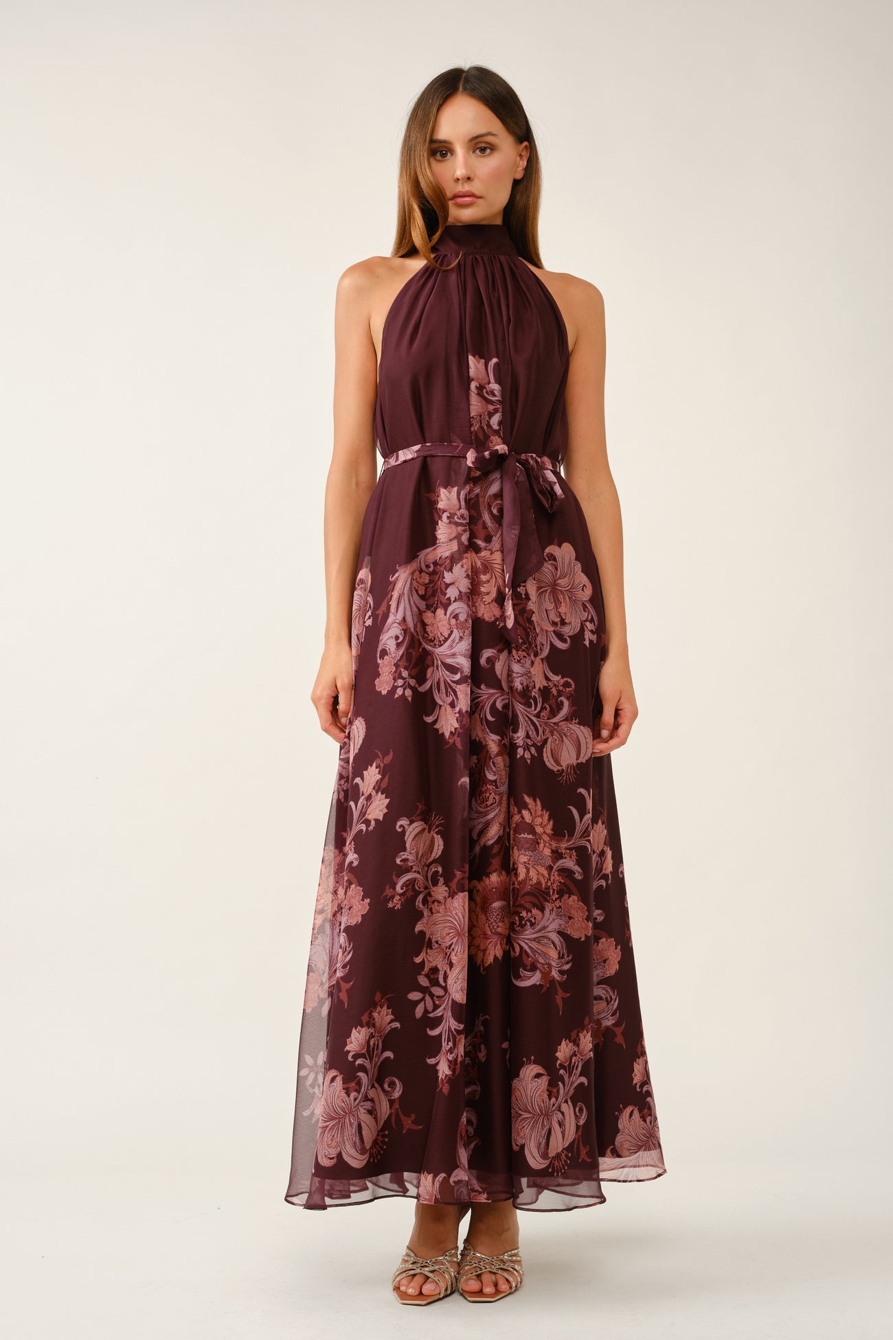 woman wearing a burgundy floral maxi dress with a halter neck and a tie waist detail