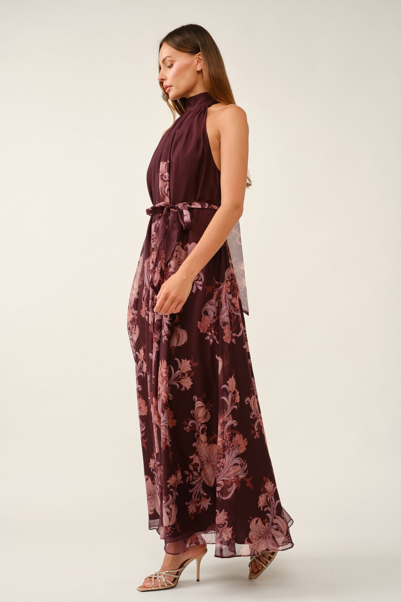 woman wearing a burgundy floral maxi dress with a high neck and tie waist detailing