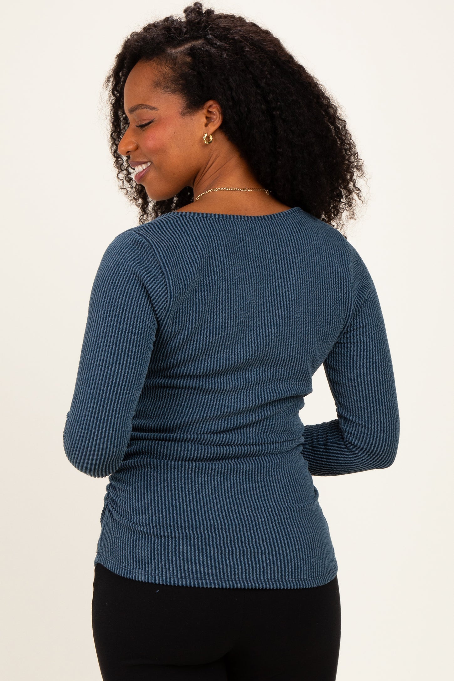 woman wearing a dark blue ribbed long sleeve top, showing the back view with a fitted silhouette