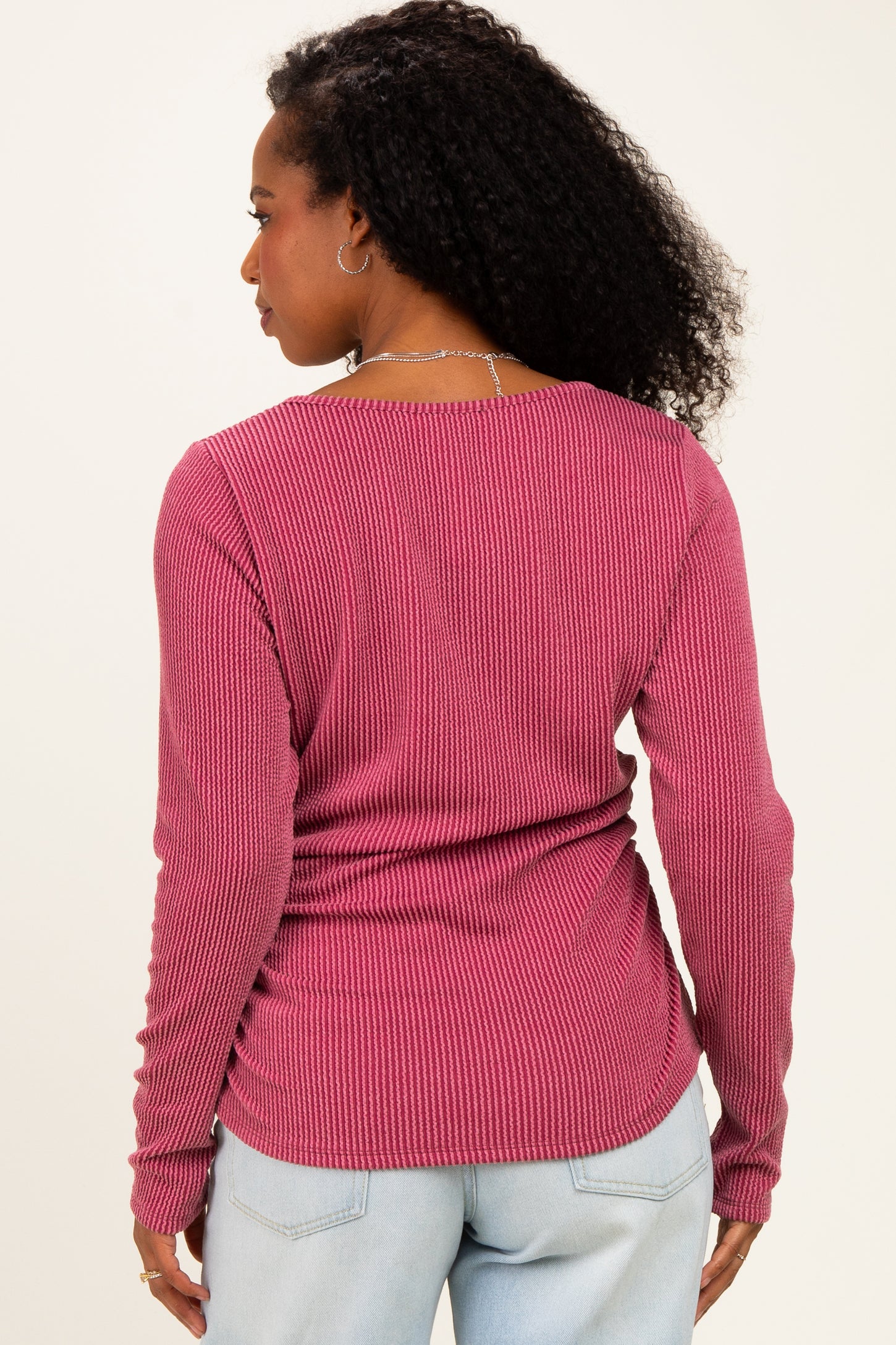 woman wearing a rose pink ribbed long sleeve top, seen from the back with her curly hair cascading down