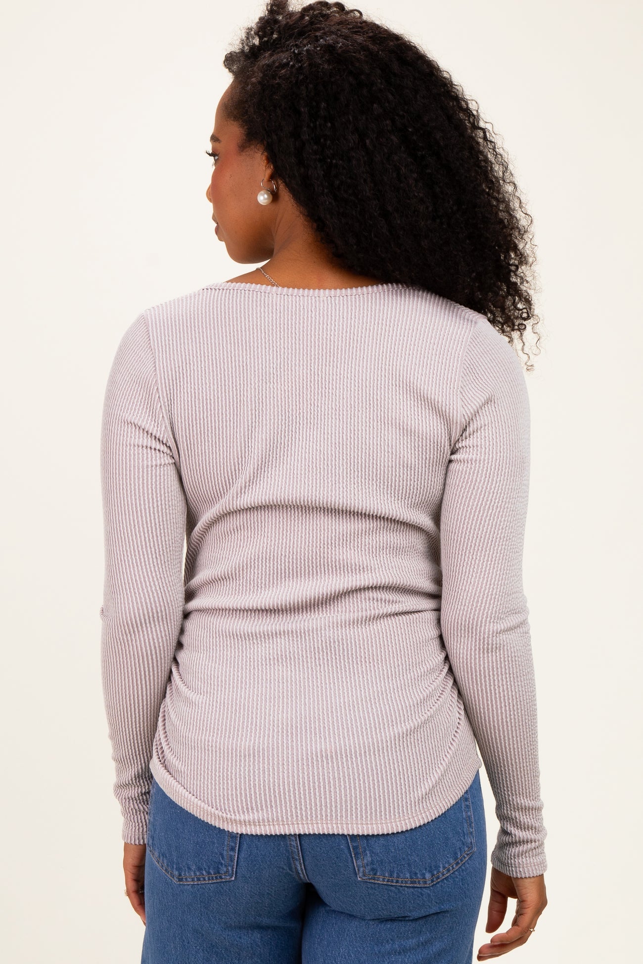woman wearing a light gray long sleeve ribbed top with a curved hem and ruched sides, viewed from the back