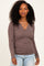 woman wearing a taupe ribbed long sleeve top with a v-neckline and ruched sides, styled with blue jeans