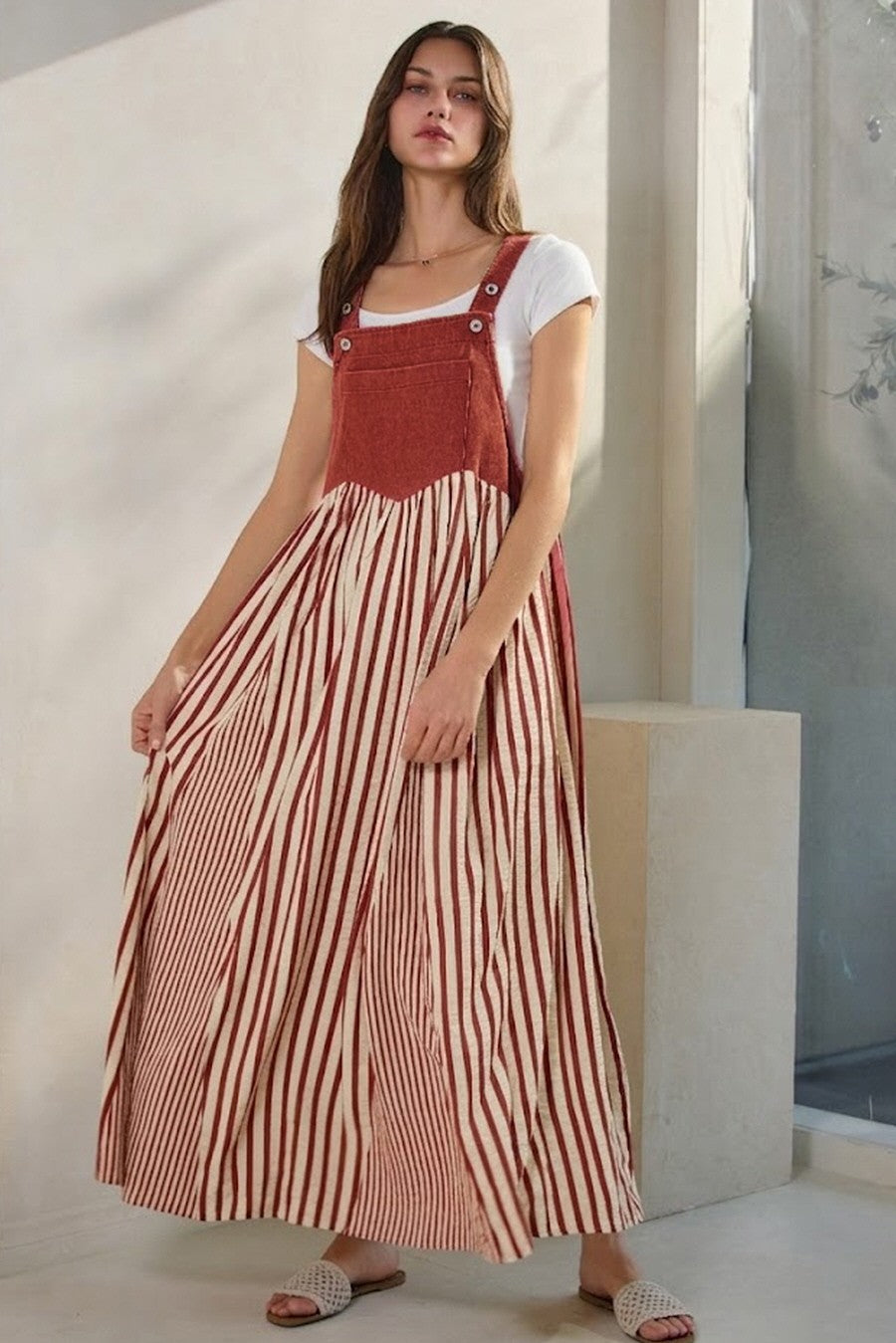 woman wearing a rust-colored striped maxi dress with a white t-shirt underneath and holding the skirt lightly