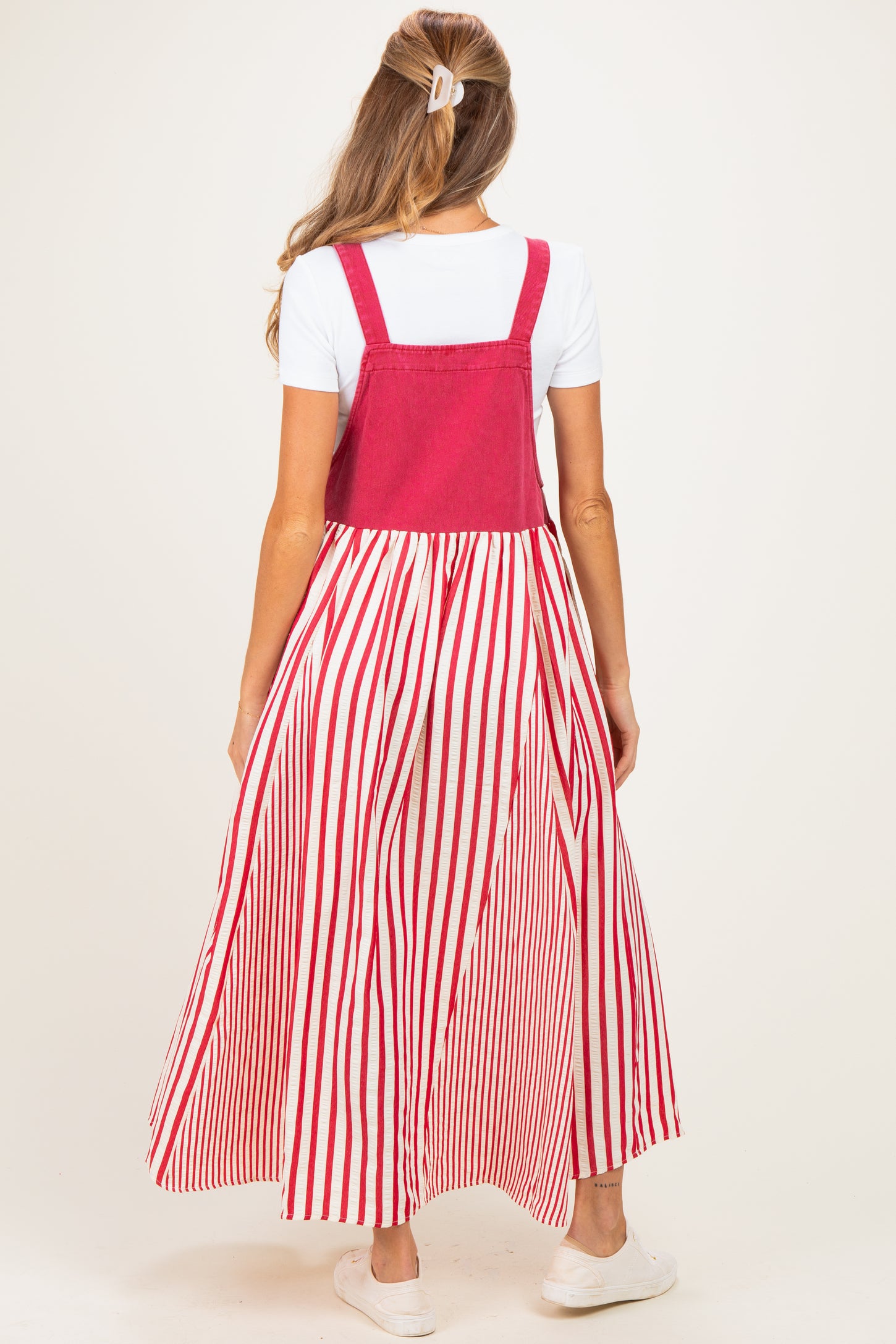 woman wearing a pink maternity maxi dress with white and red vertical stripes and a fitted top, showing her baby bump