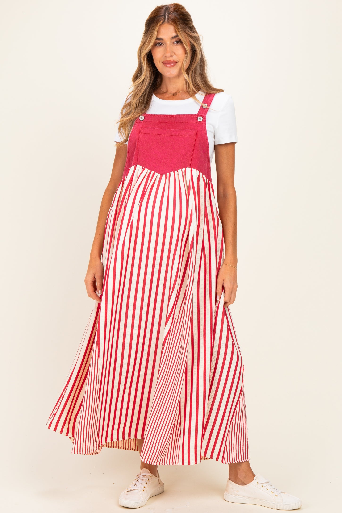 woman wearing a red and white striped maternity maxi dress with adjustable straps over a white t-shirt and white sneakers