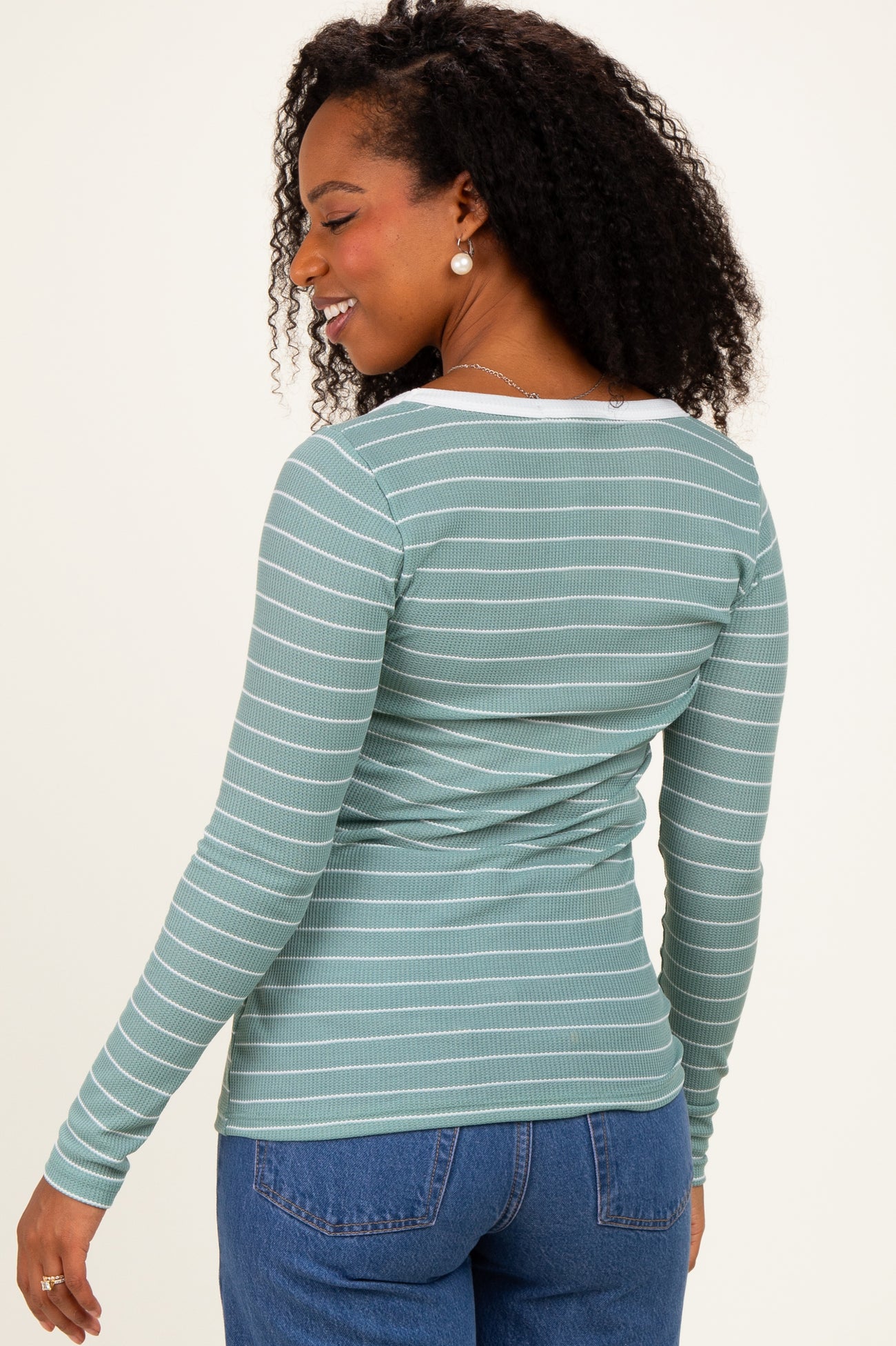 woman wearing a green and white striped long sleeve top, showing the back view with a fitted style and round neckline