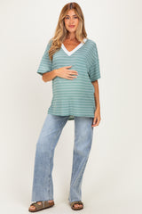 woman wearing a green striped maternity top with a v-neck and holding her baby bump, paired with light blue wide-leg jeans
