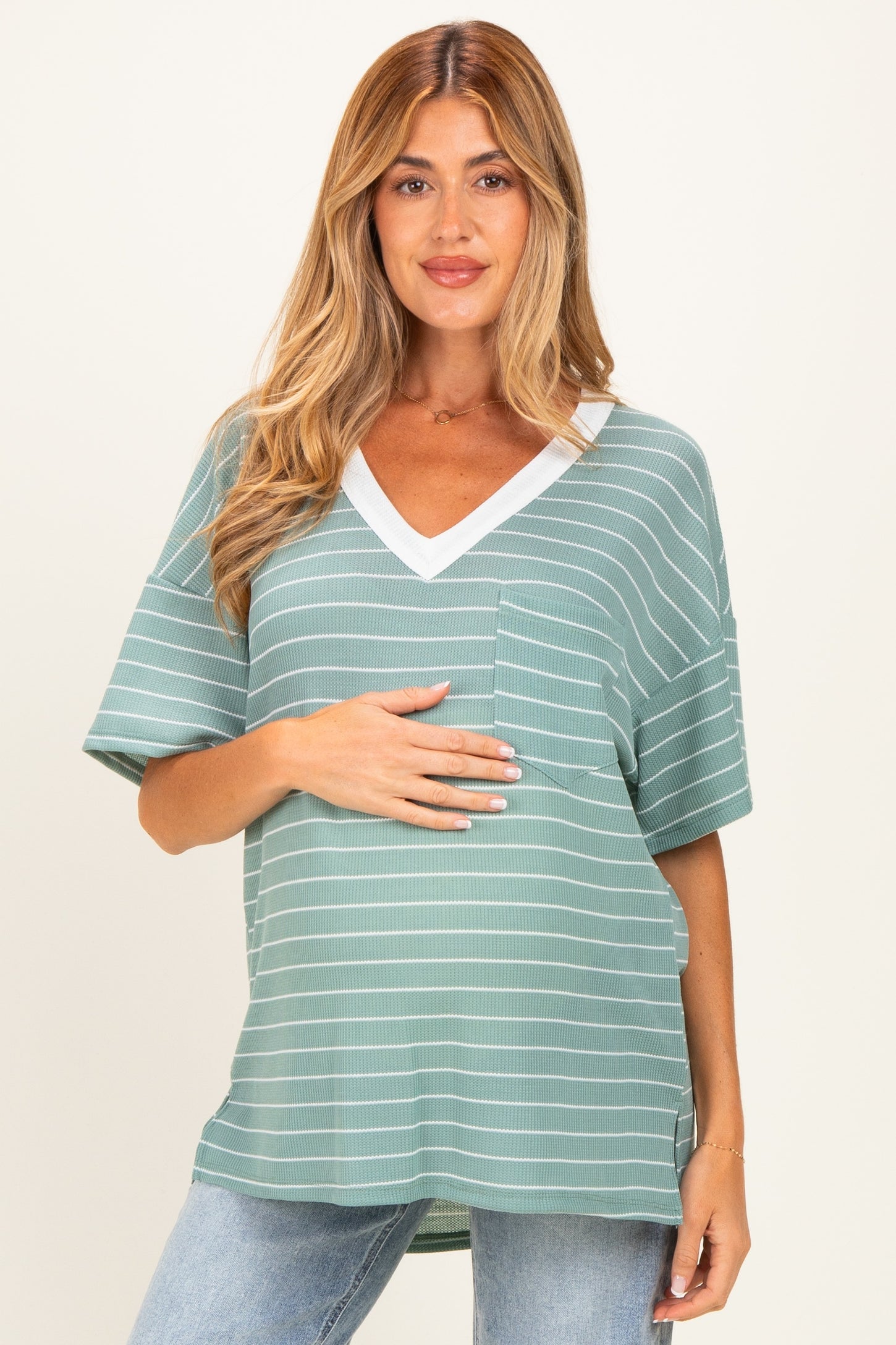 woman wearing a green striped maternity top with a v-neck and pocket, highlighting her baby bump
