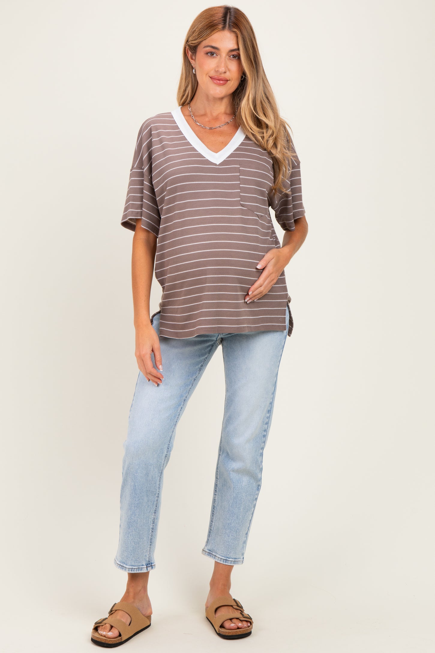 woman wearing a brown striped maternity top with a white v-neck and a visible baby bump, paired with light blue jeans