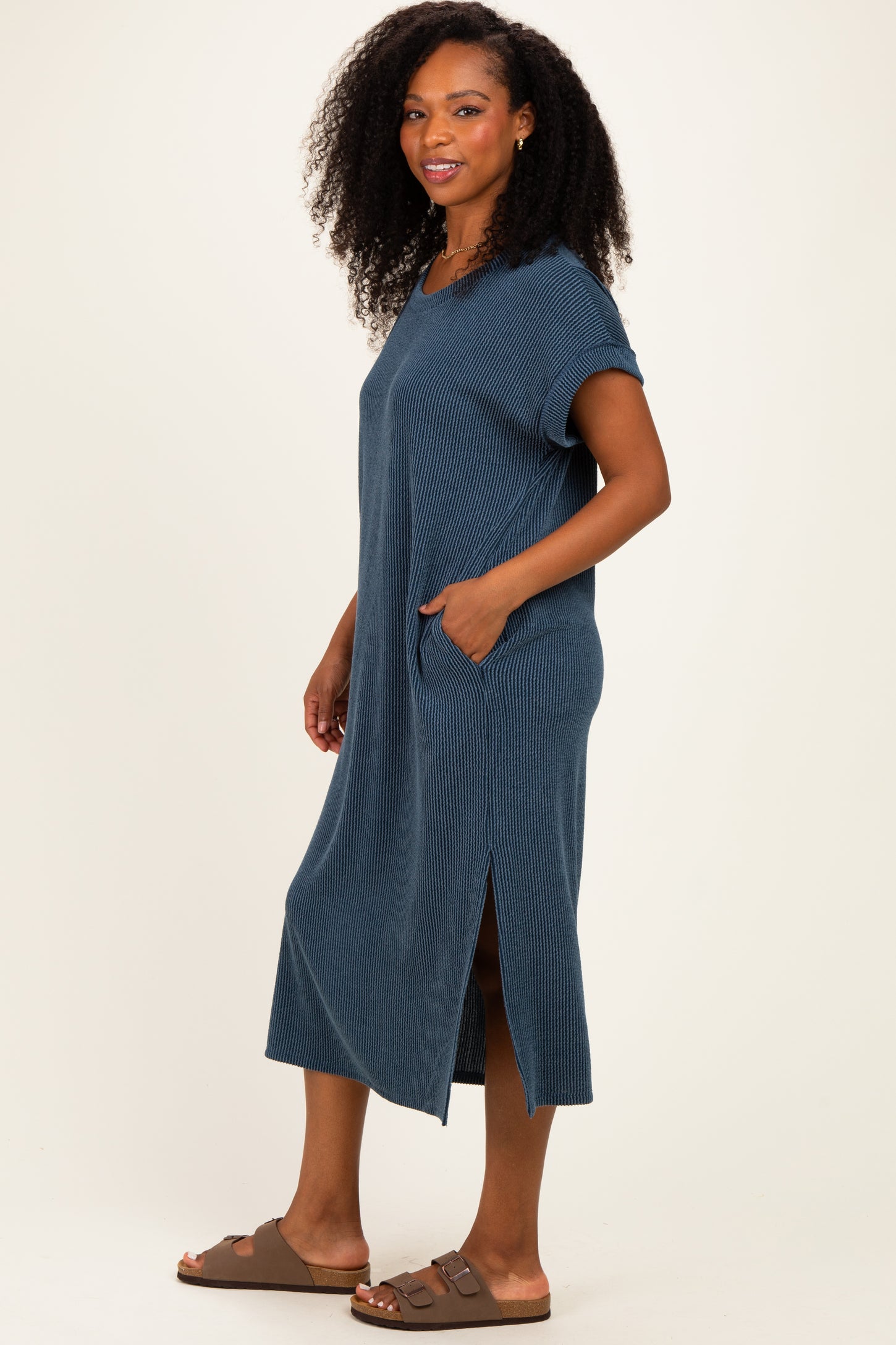 woman wearing a dark blue ribbed midi dress with short sleeves and pockets, styled with brown slide sandals