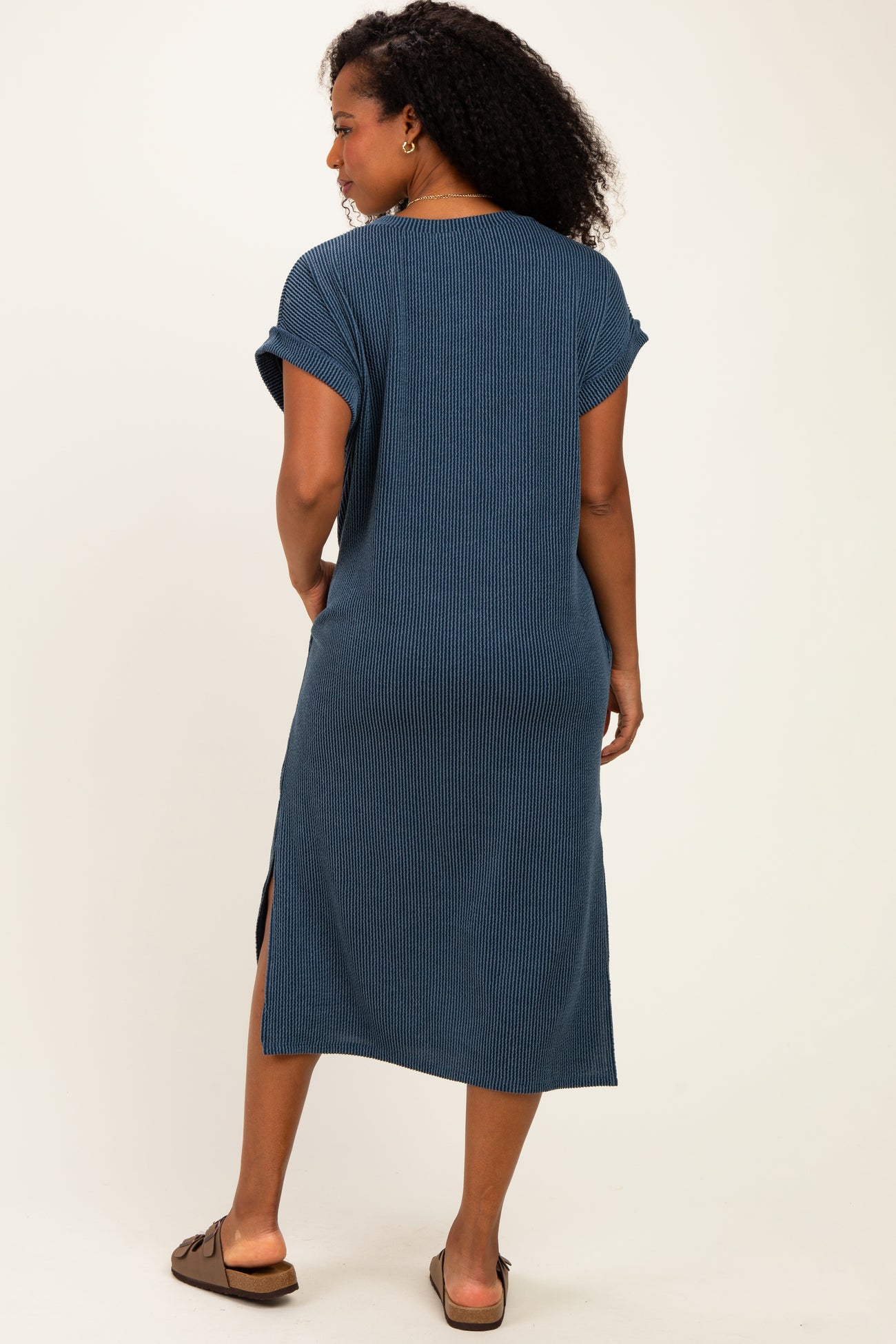woman wearing a blue ribbed midi dress with short sleeves and side slits, posing from the back