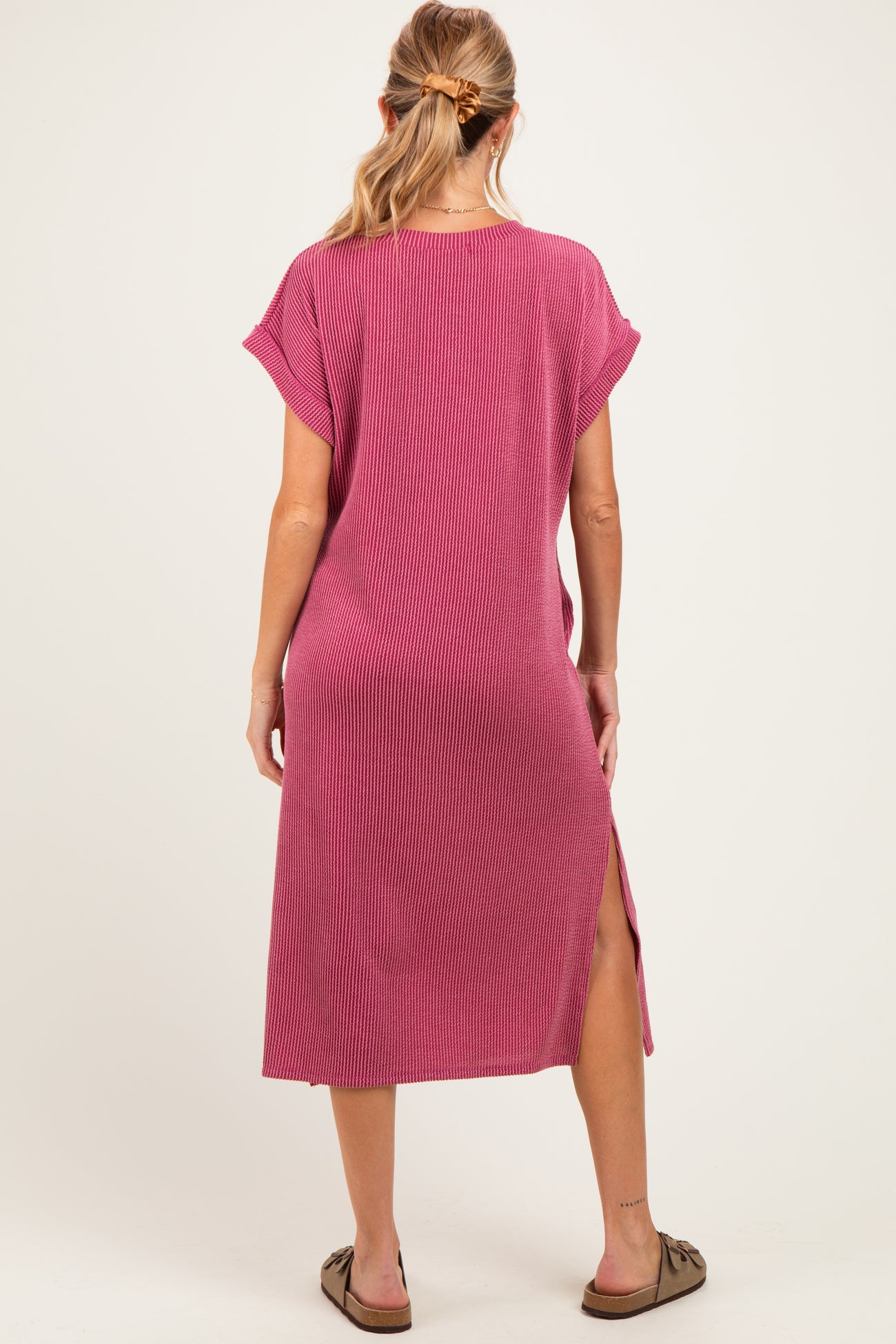 woman wearing a raspberry pink ribbed maternity maxi dress with side slits and short sleeves, seen from the back
