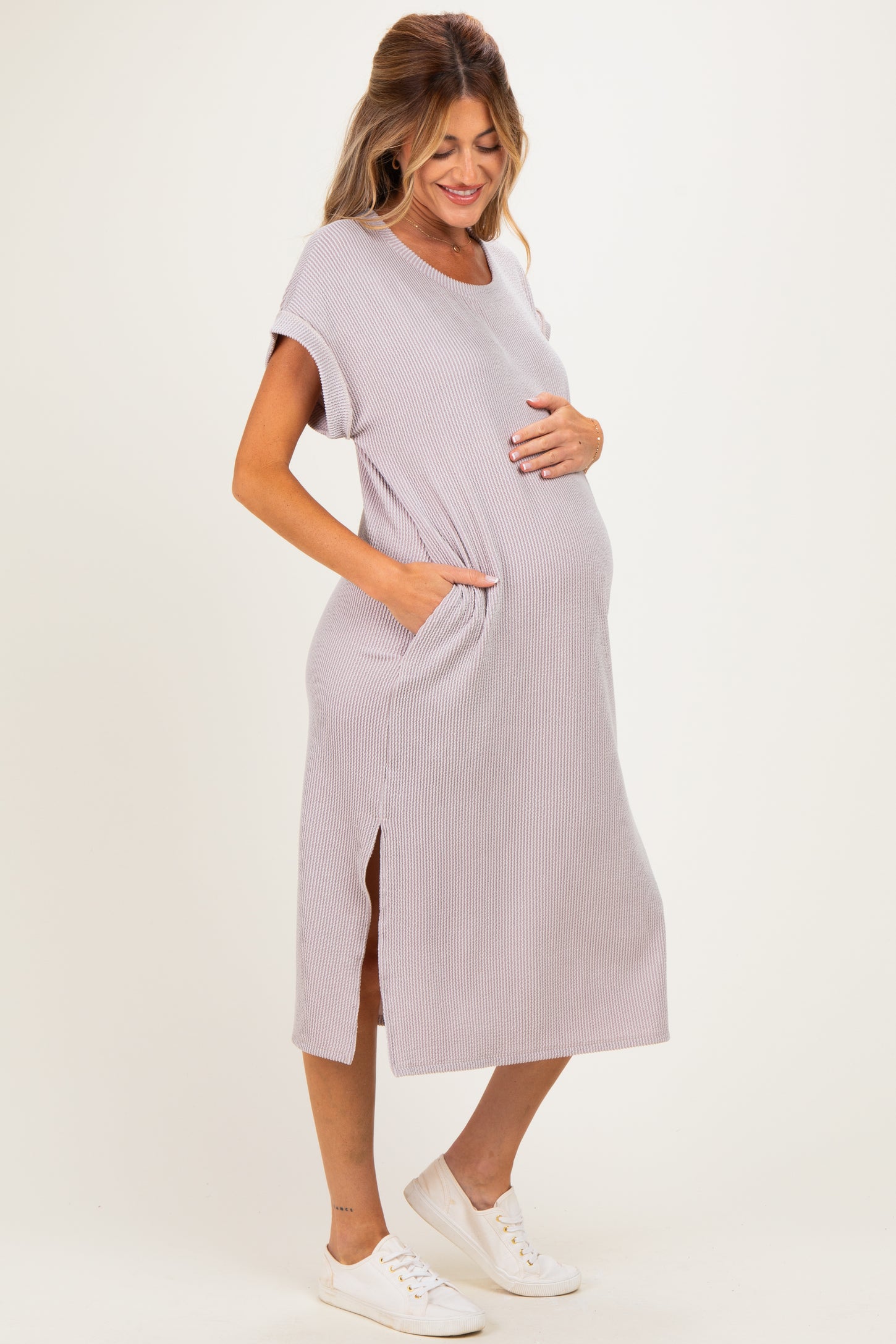 woman wearing a light purple maternity dress with pockets and side slits, gently cradling her baby bump