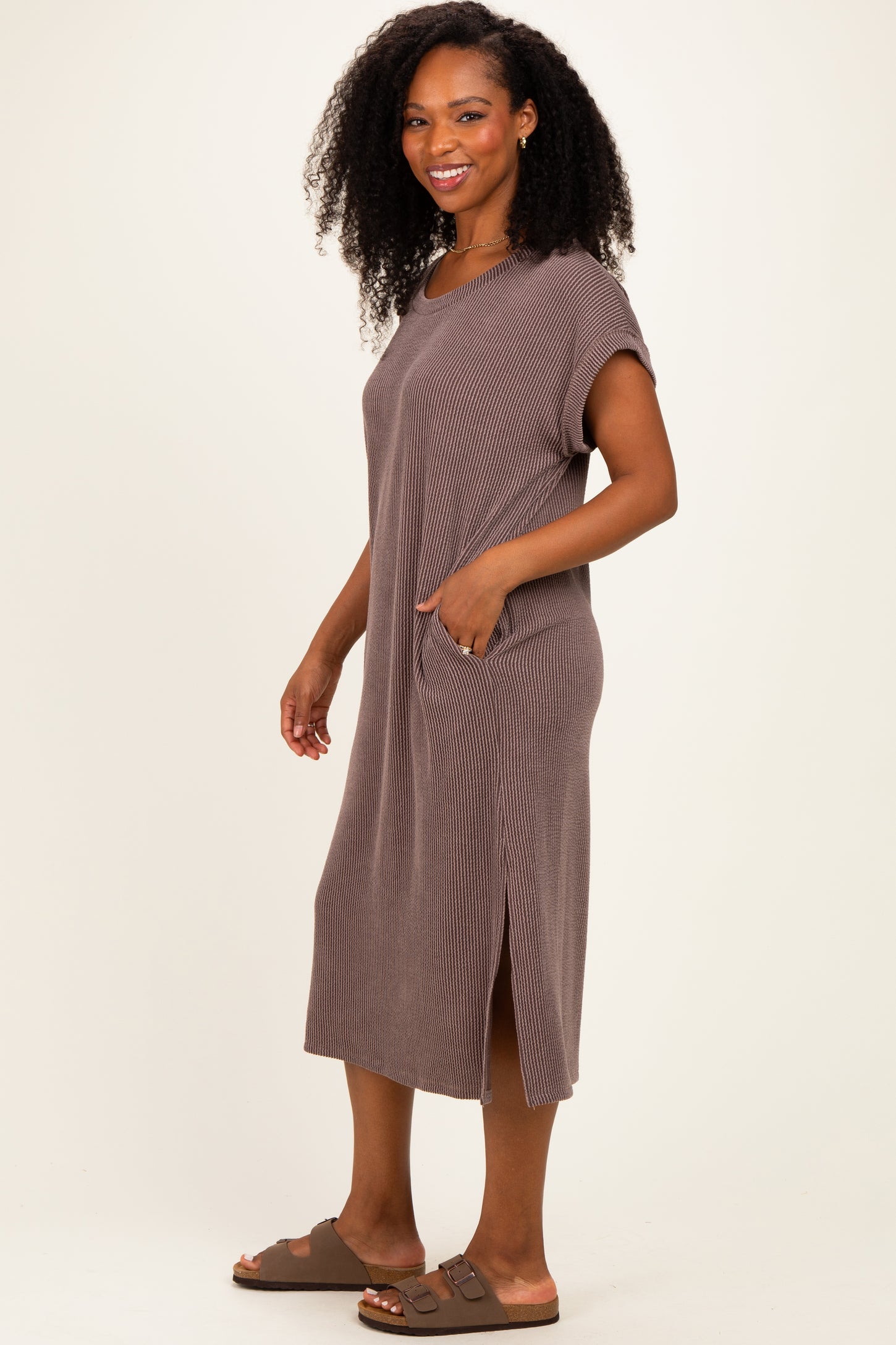 woman wearing a brown ribbed short sleeve midi dress with pockets and side slits, standing and smiling