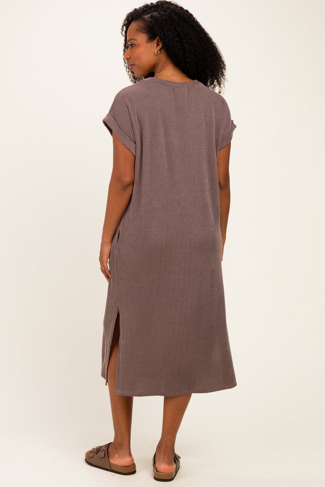 woman wearing a brown striped midi dress with short sleeves and side slits, standing with her back to the camera