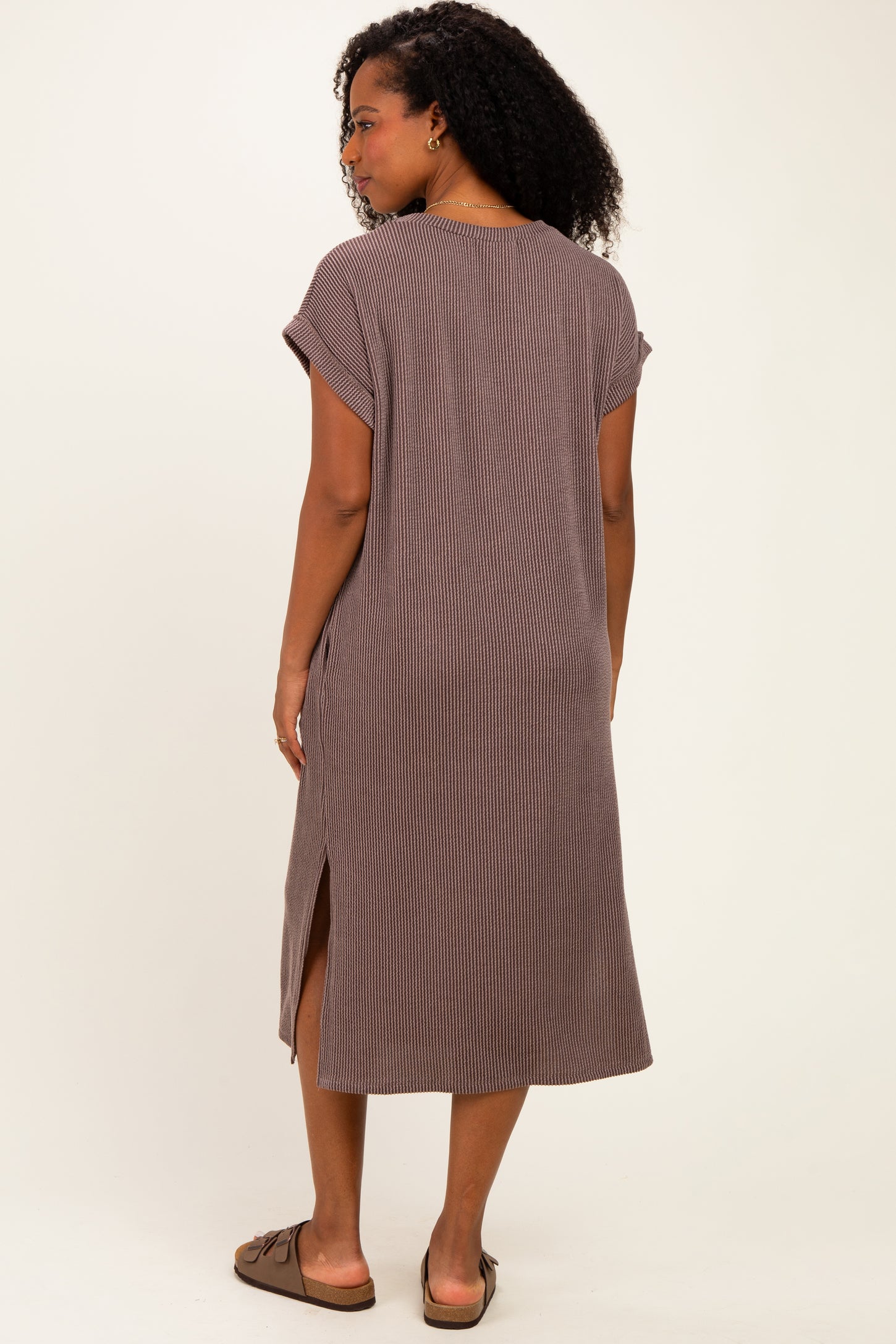 woman wearing a brown striped midi dress with short sleeves and side slits, standing with her back to the camera