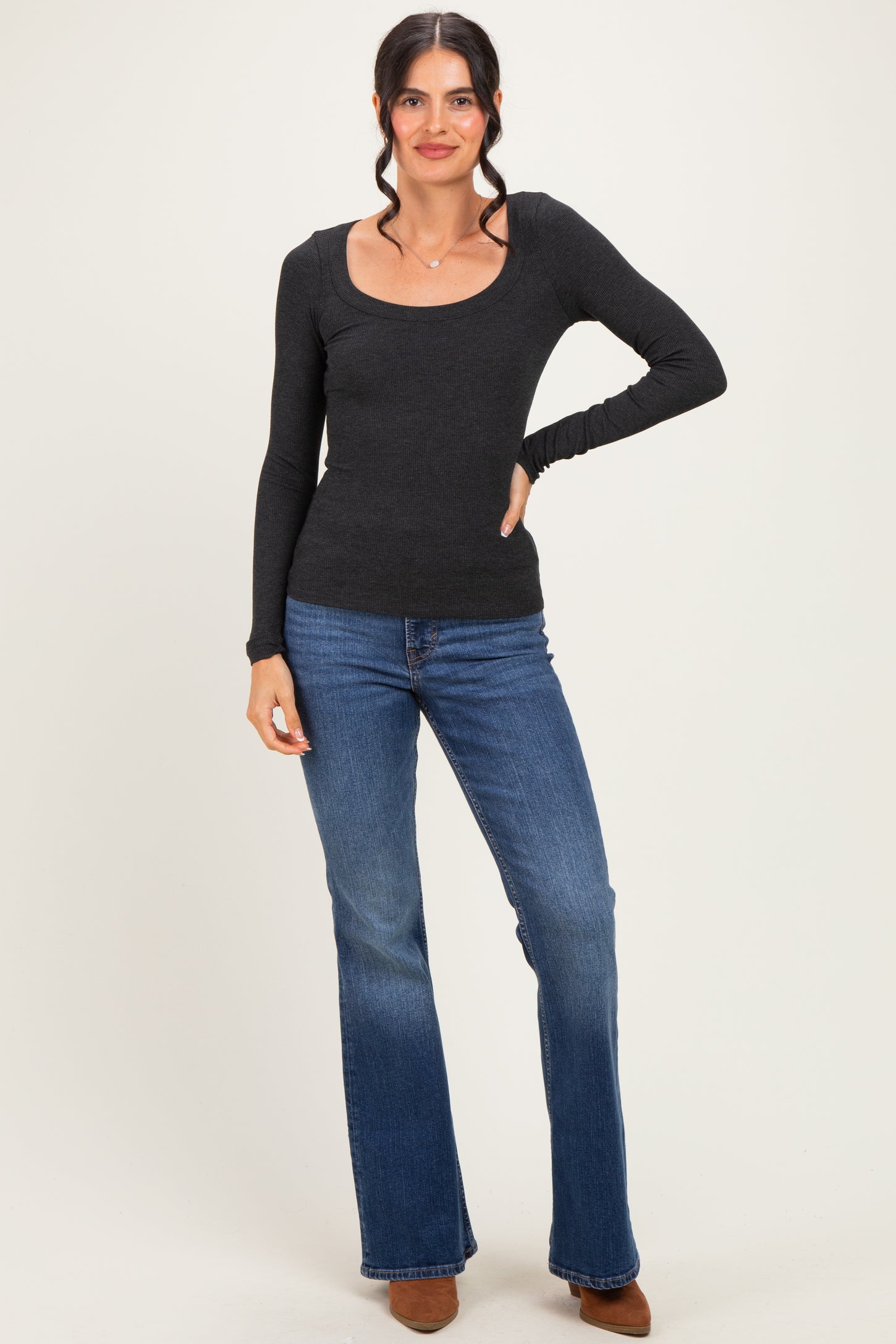 woman wearing a black long sleeve scoop neck top and flare jeans, standing with one hand on her hip