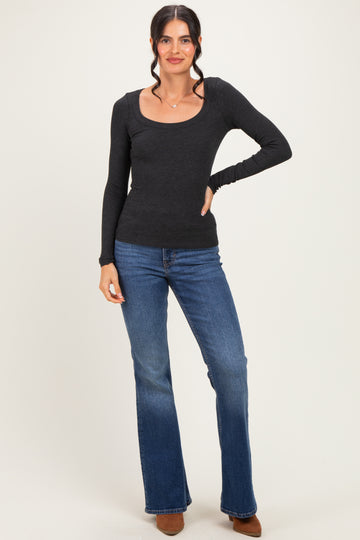 woman wearing a black long sleeve scoop neck top and flare jeans, standing with one hand on her hip