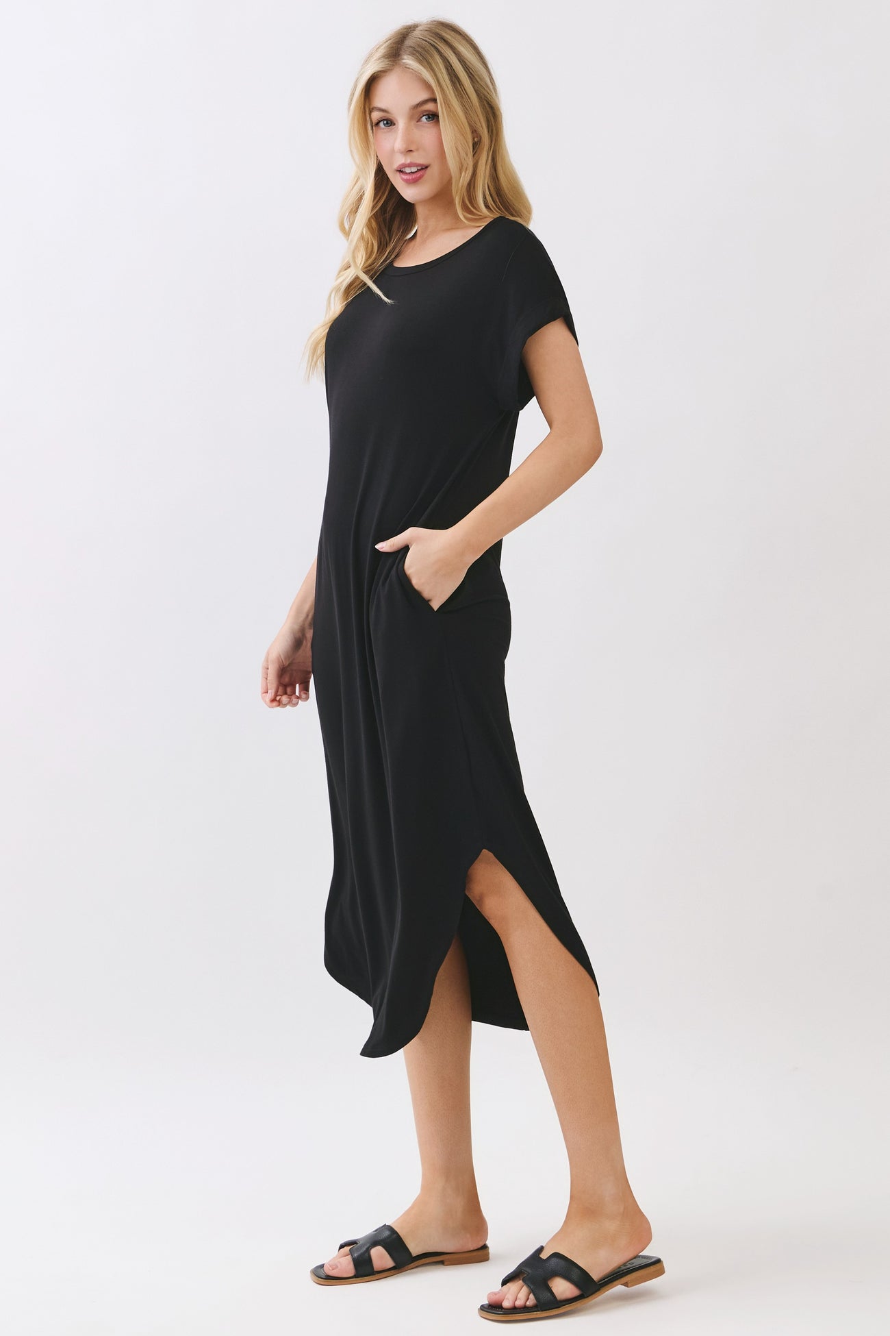 woman wearing a black midi dress with short sleeves and side pockets, standing in a relaxed pose
