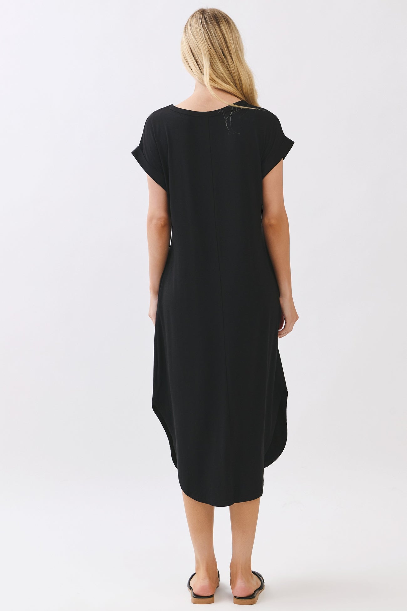 woman wearing a black short sleeve dress with a curved hem and relaxed fit, viewed from the back