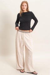 woman wearing a black long sleeve top with asymmetrical design and light beige wide-leg pants with drawstring waist