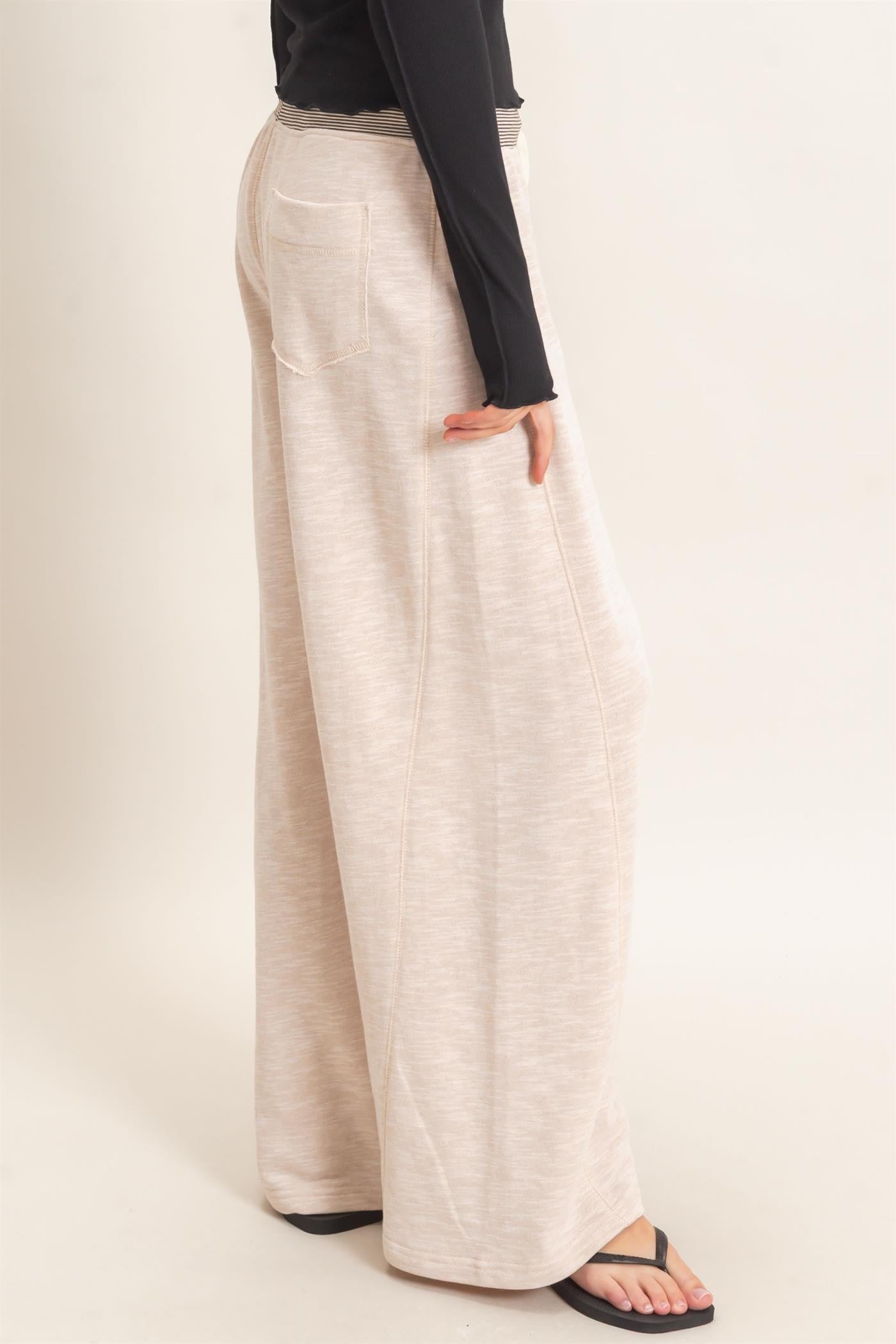 woman wearing light beige wide-leg pants with a high waist and back pockets, styled casually with a long sleeve top