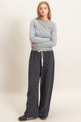 woman wearing a gray long sleeve top with an asymmetrical neckline and black wide-leg pants with a drawstring waist