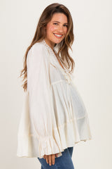 woman wearing a cream maternity blouse with ruffled sleeves and a relaxed fit, showcasing her baby bump