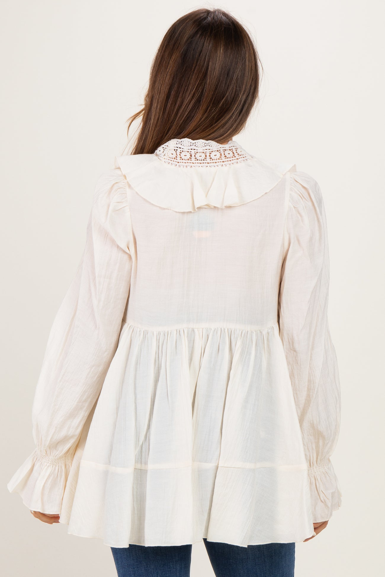woman wearing a cream maternity top with a ruffled collar and long sleeves, showing a flowing silhouette from the back