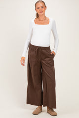 woman wearing a white long sleeve maternity top and brown wide-leg maternity pants, showing her baby bump