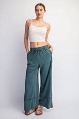 woman wearing a white crop top and teal wide-leg pants with pockets and drawstring waist