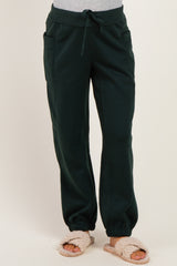 woman wearing dark green maternity jogger pants with an elastic waistband and pockets, styled with fuzzy slippers