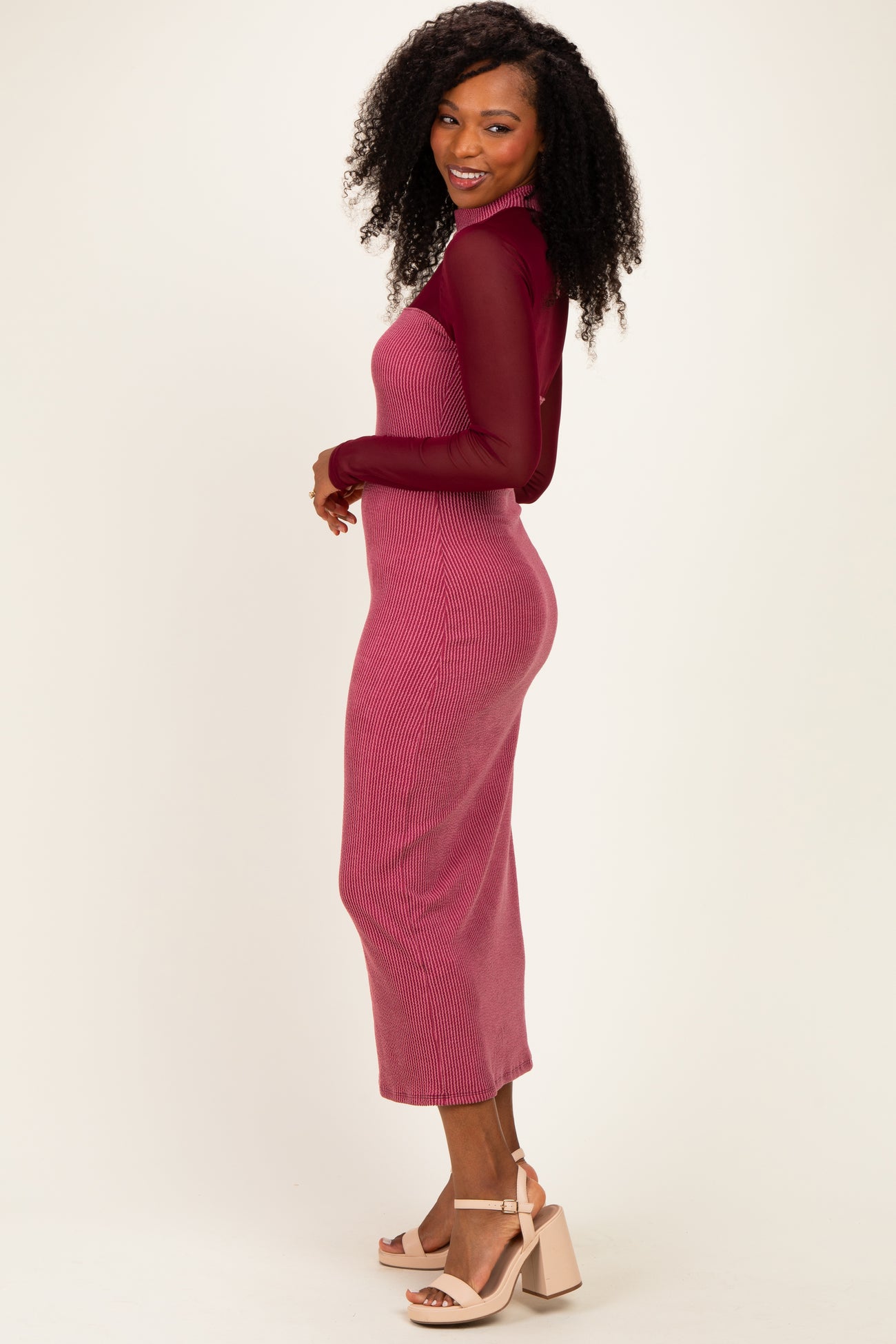 woman wearing a burgundy ribbed knit midi dress with sheer long sleeves and blush heeled sandals