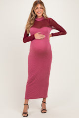 woman wearing a maroon ribbed maternity dress with sheer sleeves and holding her baby bump
