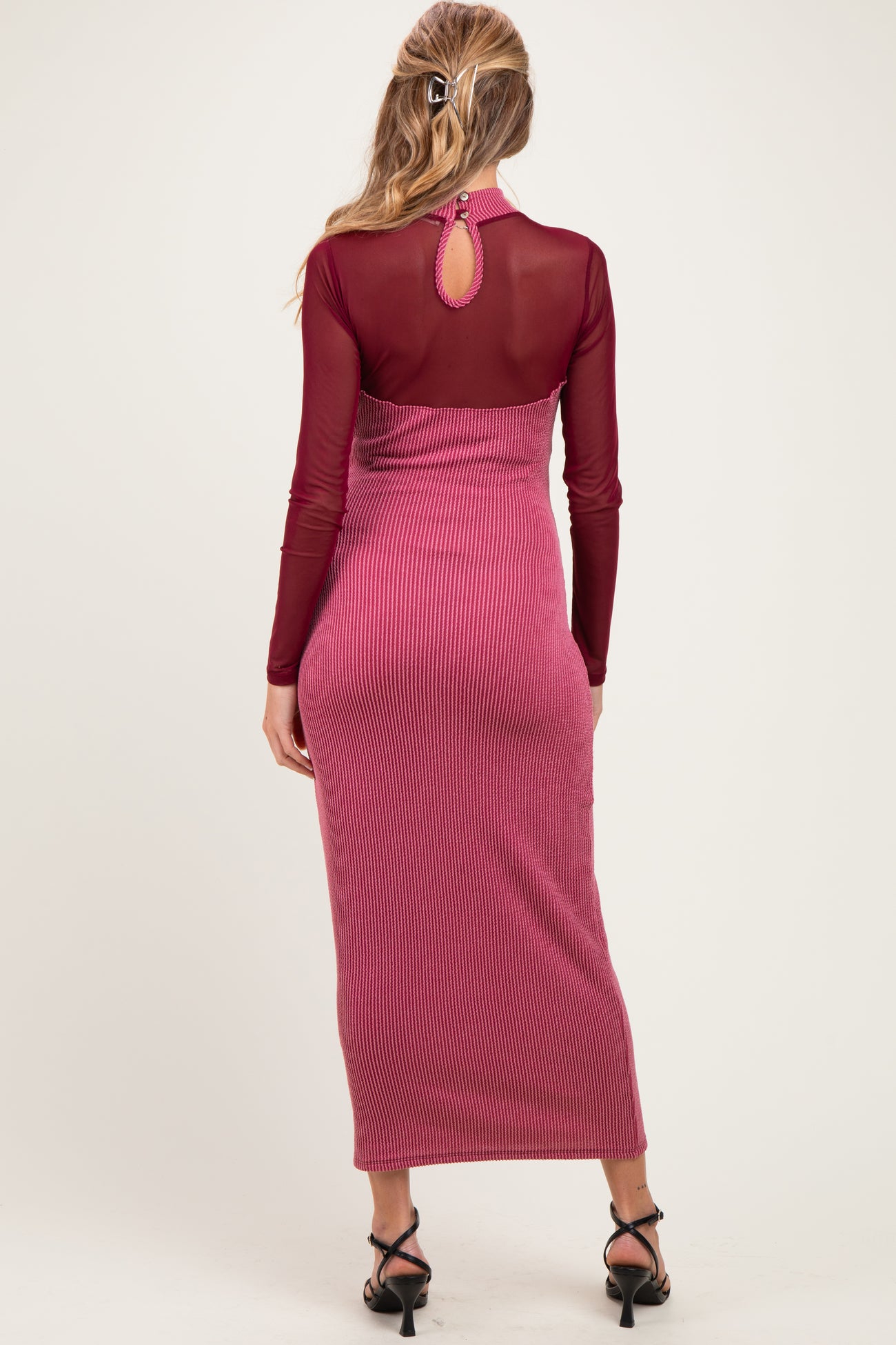 woman wearing a burgundy maternity dress with a sheer back and ribbed texture, styled with strappy heels