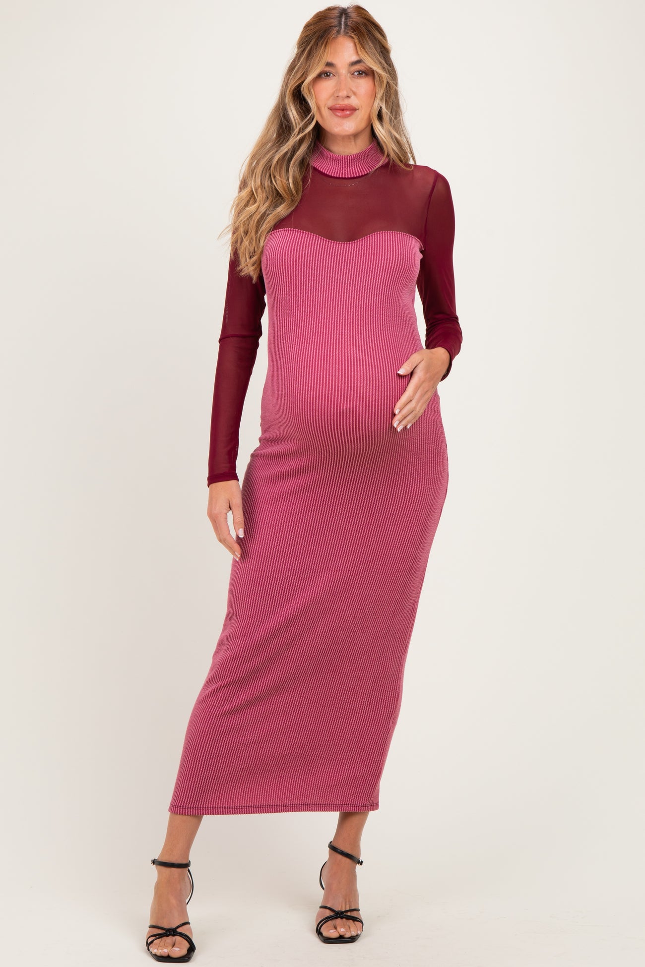 woman wearing a burgundy ribbed maternity dress with a sheer long sleeve top and a visible baby bump