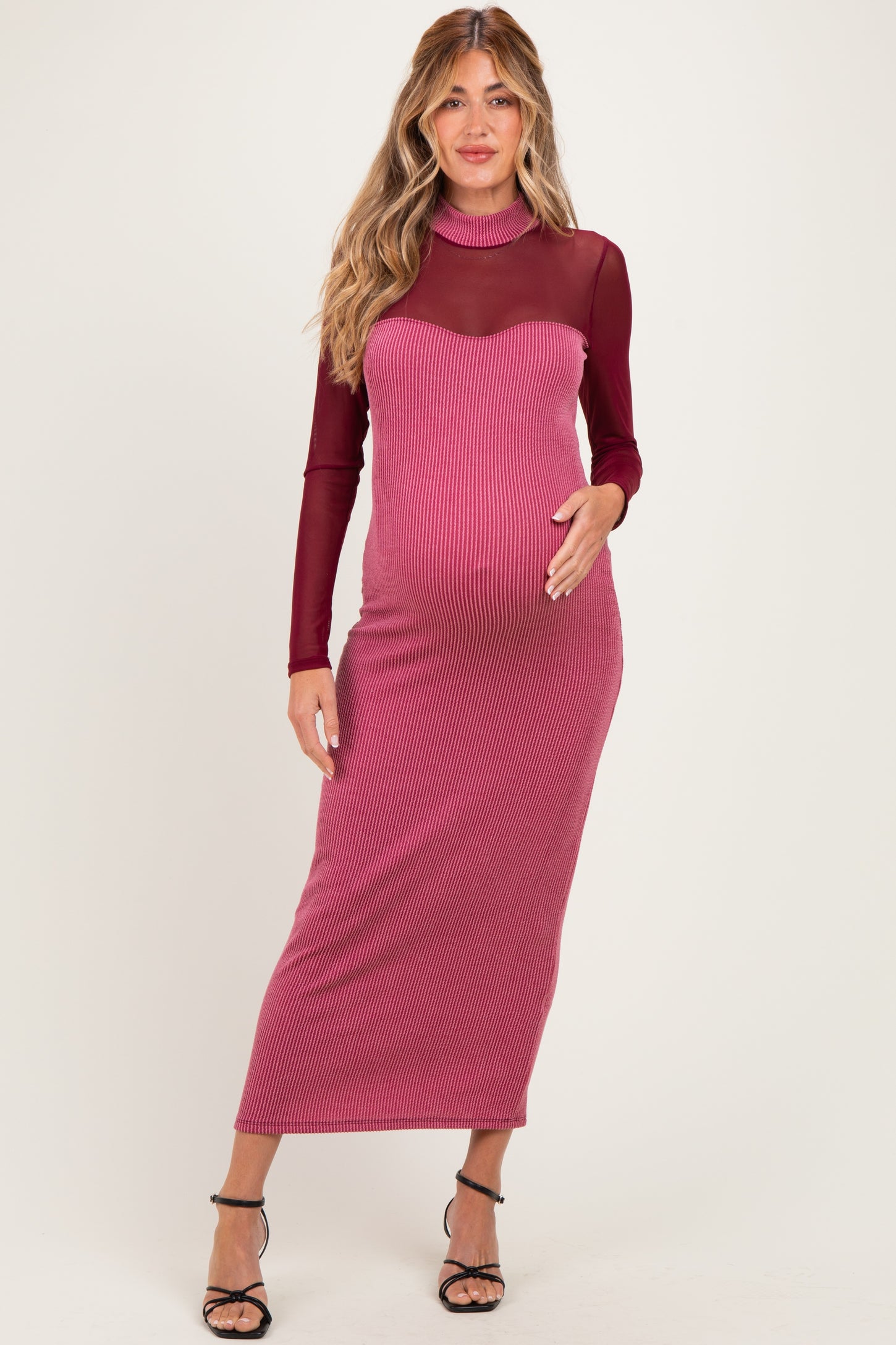 woman wearing a burgundy ribbed maternity dress with a sheer long sleeve top and a visible baby bump