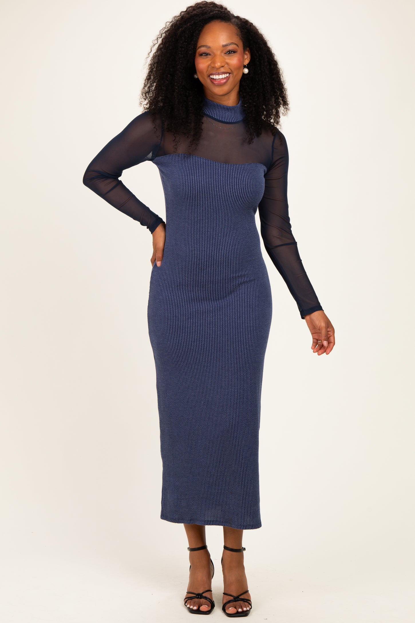 woman wearing a navy striped long sleeve midi dress with a sheer neckline and black strappy heels