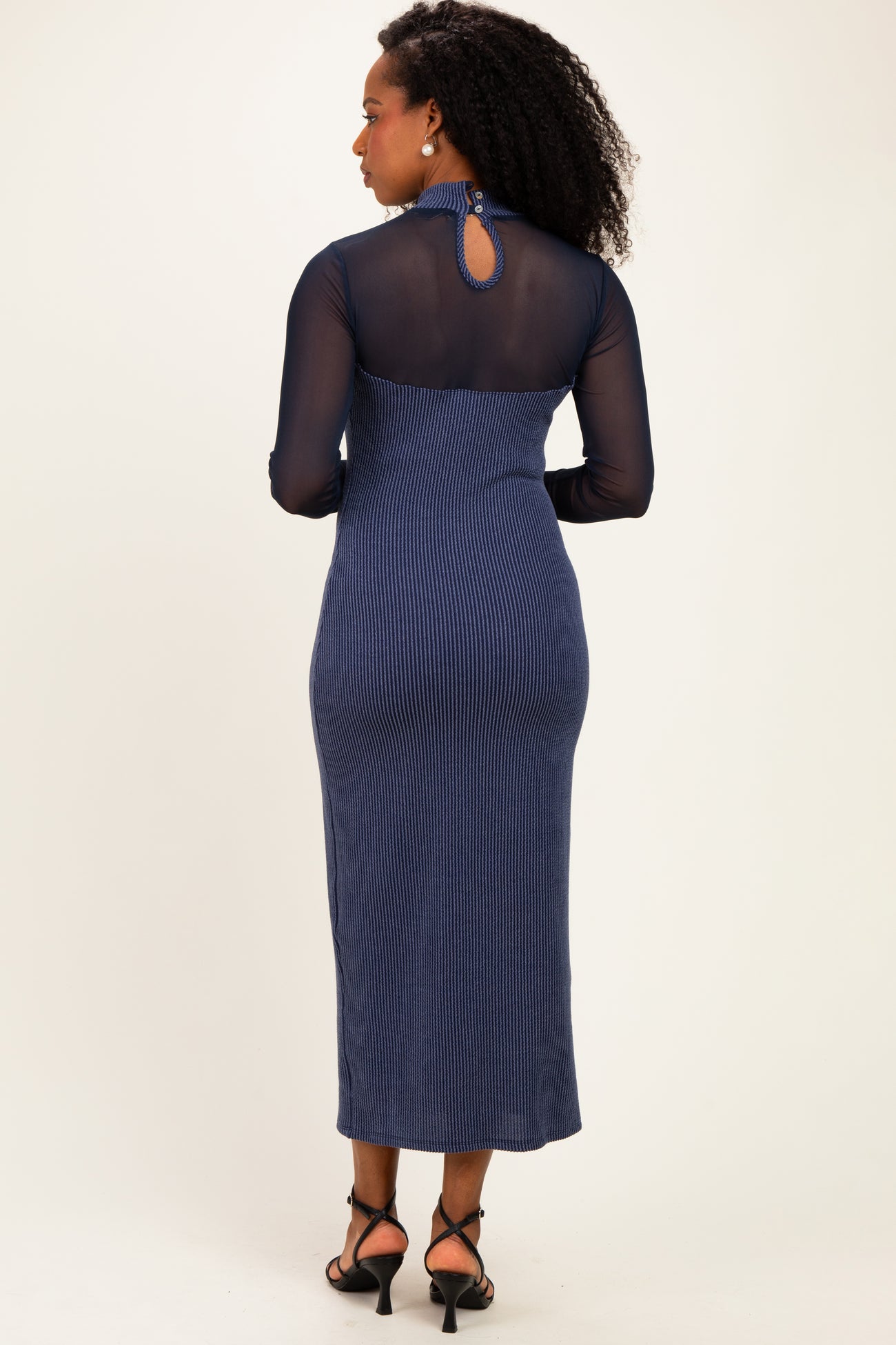 woman wearing a navy blue ribbed midi dress with long sheer sleeves and a keyhole back detail
