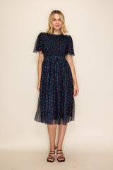 woman wearing a navy blue midi dress with floral print and puff sleeves, styled with black strappy sandals