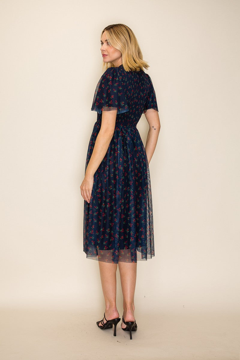 woman wearing a navy blue floral midi dress with sheer overlay, standing with her back to the camera