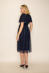woman wearing a navy blue floral midi dress with sheer overlay, standing with her back to the camera