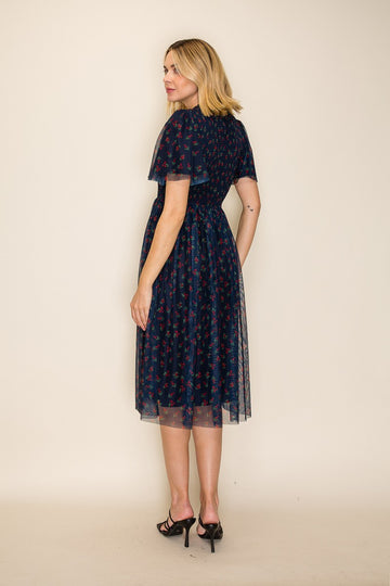 woman wearing a navy blue floral midi dress with sheer overlay, standing with her back to the camera