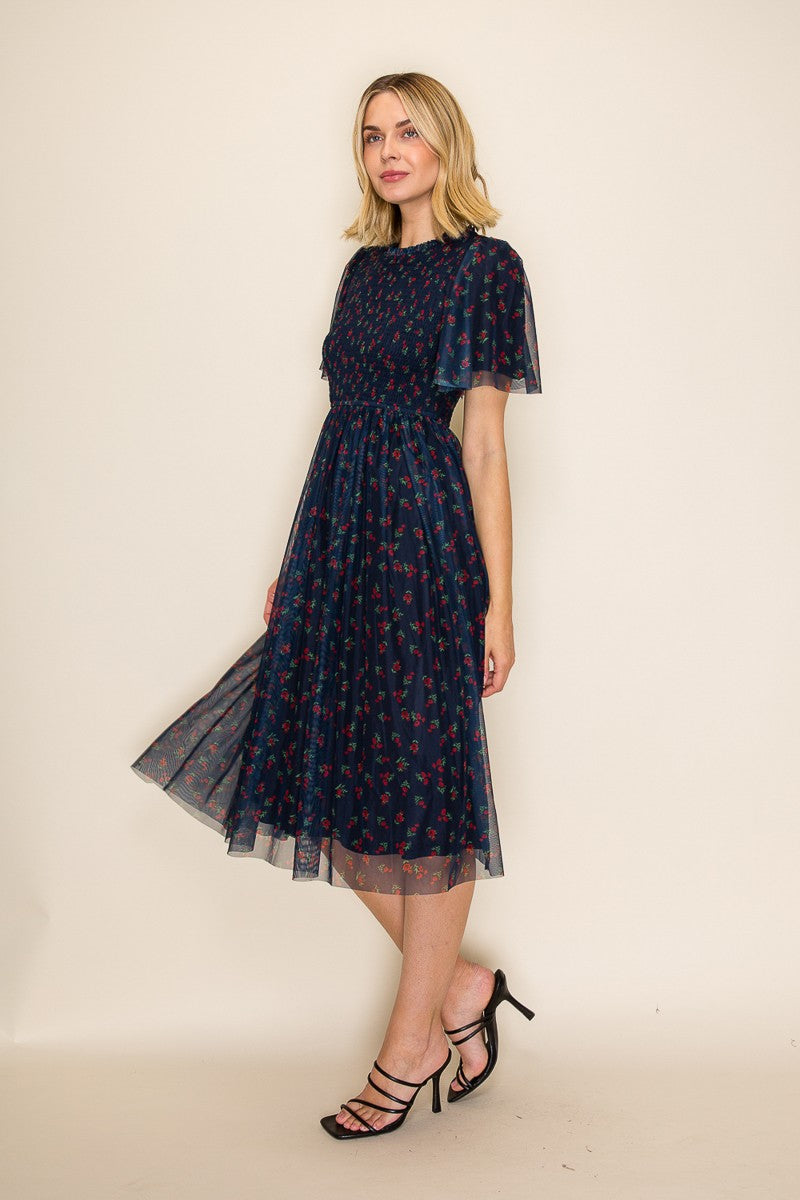 woman wearing a navy blue floral midi dress with a sheer overlay and flutter sleeves, styled with black strappy heels
